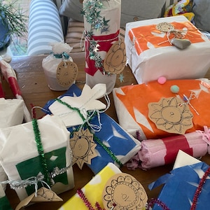 May include: A collection of wrapped gifts in various shapes and sizes, adorned with decorative tags and embellishments. The gifts are wrapped in white, blue, orange, and yellow paper, with accents of green and silver tinsel. Some tags have numbers.
