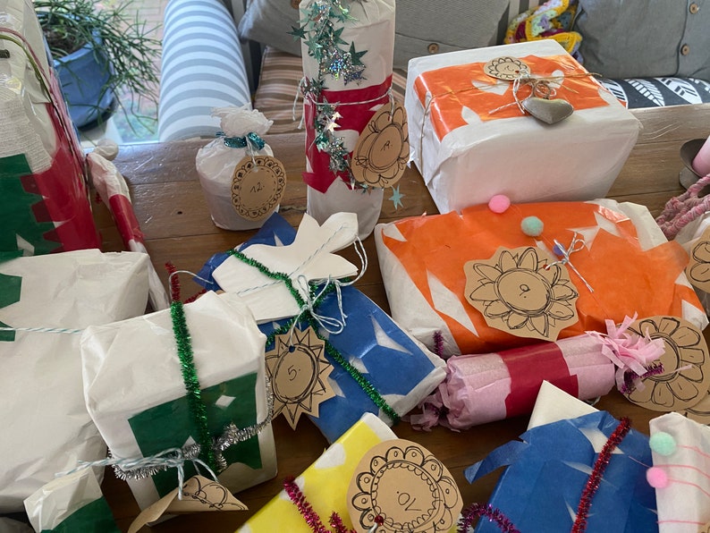 May include: A collection of wrapped gifts in various shapes and sizes, adorned with decorative tags and embellishments. The gifts are wrapped in white, blue, orange, and yellow paper, with accents of green and silver tinsel. Some tags have numbers.