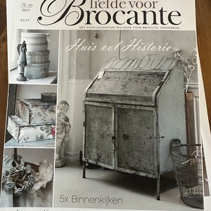 Könnte beinhalten: Ein Magazincover mit einem Vintage-Metallschrank mit Drahtgitterdesign. Das Magazin trägt den Titel "liefde voor Brocante" und der Text "Huis vol Historie" ist ebenfalls sichtbar. Das Magazin handelt von Einrichtung und Vintage-Artikeln.