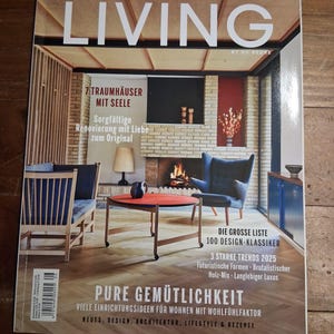 May include: A magazine cover titled "SCANDINAVIAN LIVING" features a living room interior with a fireplace, blue armchair, and a red coffee table. Text includes "7 Traumhäuser mit Seele" and "Pure Gemütlichkeit". The cover showcases interior design and lifestyle.