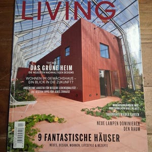 May include: A magazine cover titled "Scandinavian Living" features a modern red house with large windows and a glass roof. Text includes "Das Grüne Heim" and "9 Fantastische Häuser". The cover showcases sustainable design and home decor.