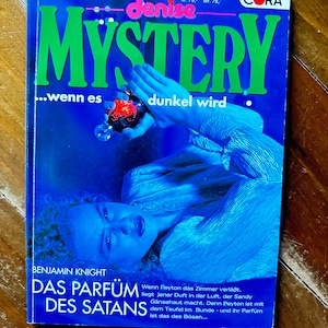 Peut inclure: Une couverture de livre bleue et verte avec le titre "MYSTERY...wenn es dunkel wird" et le texte "DAS PARFÜM DES SATANS" en dessous. La couverture du livre présente une femme allongée les yeux fermés.