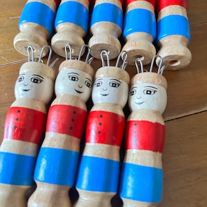 Könnte beinhalten: Satz Holzstricknadeln mit bemalten Gesichtern und rot-weiß-blauen Streifen. Die Nadeln haben Metallschlaufen oben.