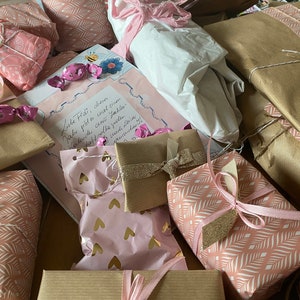 May include: An assortment of wrapped gifts in various sizes and patterns. The gifts are wrapped in pink, white, and brown paper, some with gold accents. Pink ribbons and bows adorn the packages, creating a festive and celebratory feel.