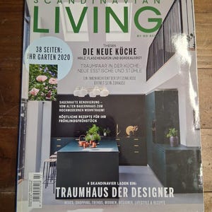 May include: A magazine cover titled "Scandinavian Living" with the text "Die Neue Küche" and "Ihr Garten 2020." The cover features a modern kitchen design with dark teal cabinetry and a central island. The magazine's theme is home design and lifestyle.