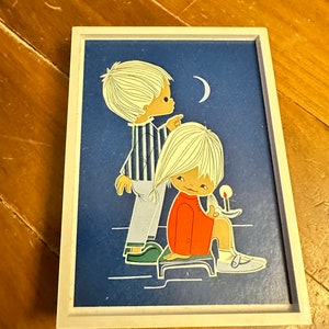 May include: A framed illustration of two children, a boy and a girl, standing in front of a blue night sky with a crescent moon. The boy is pointing at the moon and the girl is holding a candle. The illustration is in a white frame.
