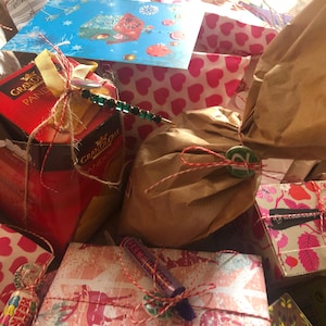 May include: A collection of wrapped gifts, some in patterned paper with hearts and floral designs. The gifts are tied with twine and ribbon, and some have decorative embellishments. A blue card with a winter scene is visible.