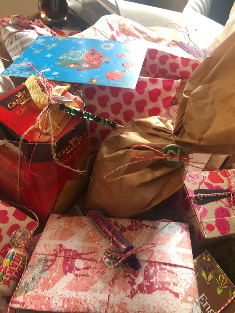 May include: A collection of wrapped gifts, some in patterned paper with hearts and floral designs. The gifts are tied with twine and ribbon, and some have decorative embellishments. A blue card with a winter scene is visible.