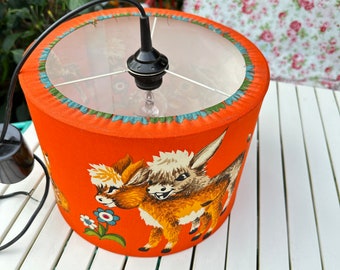 May include: Orange lampshade with a white fabric lining and a black cord. The lampshade features a whimsical design of two brown and white donkeys with flowers.