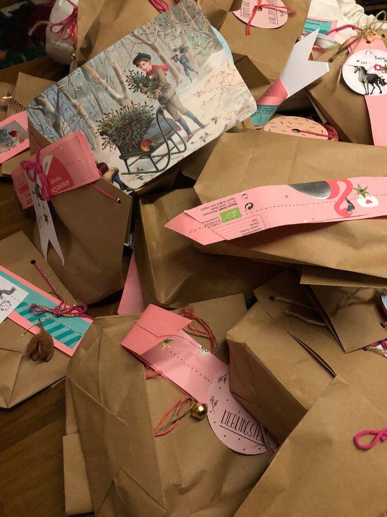 May include: A pile of brown paper gift bags, some with pink tags and string. One bag has a vintage winter scene illustration. Some tags have text and small bells. The bags are tied with pink and brown string.