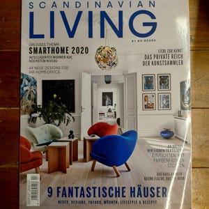 May include: A magazine cover featuring a Scandinavian home design theme. The cover features a photo of a living room with a blue, red, and green armchair, a light wood floor, and a large window. The magazine title is "Scandinavian Living" and the text "Smarthome 2020" is featured in the upper left corner.