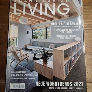 May include: A magazine cover titled "SCANDINAVIAN LIVING" with interior design themes. The cover features a modern living room with a gray sofa, wooden furniture, and a plant. Text includes "NEUE WOHNTRENDS 2021".