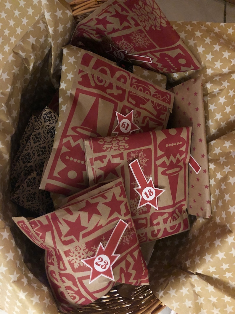May include: A wicker basket filled with Advent calendar bags. The bags are brown with a red holiday-themed pattern and star-shaped number tags. The basket is lined with star-patterned paper.