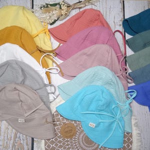 Könnte beinhalten: Eine Kollektion von Sonnenhüten aus strukturiertem Musselinstoff in verschiedenen Farben, darunter Gelb, Senf, Weiß, Grau, Beige, Koralle, Rosa, Mint, Türkis, Blau und Petrol. Jeder Hut verfügt über eine breite Krempe und Kinnbänder.
