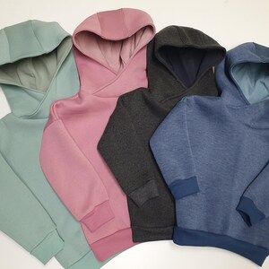 Könnte beinhalten: Vier Kapuzenpullover in verschiedenen Farben: hellgrün, rosa, dunkelgrau und blau. Die Pullover haben ein Crossover-Kapuzendesign.