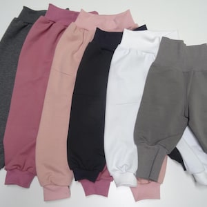 Könnte beinhalten: Eine Auswahl an Babyhosen in verschiedenen Farben, darunter Grau, Rosa, Schwarz und Weiß. Die Hosen haben einen hohen Bund und geraffte Knöchel und bieten ein komfortables und stilvolles Design für Babys und Kleinkinder.