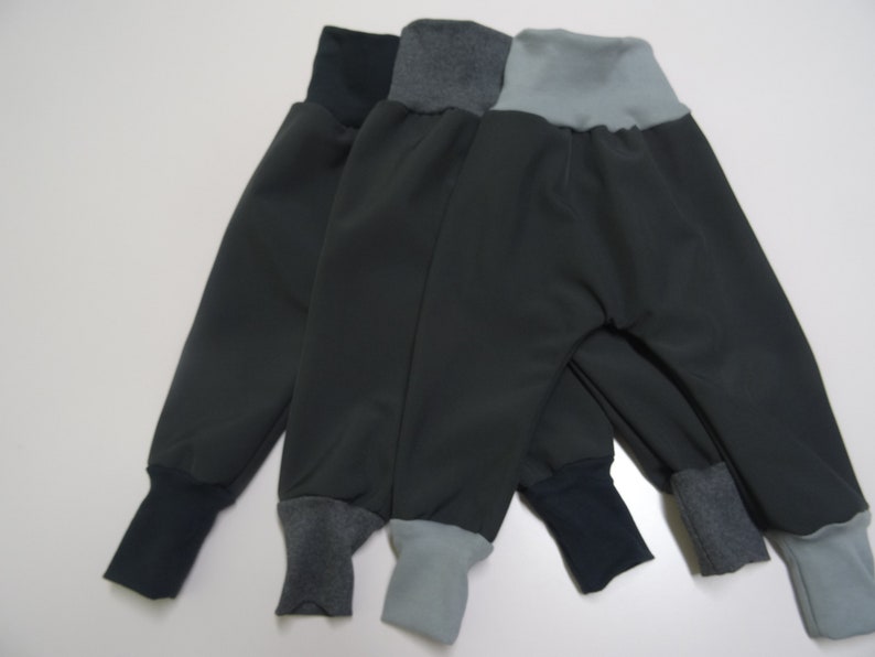 May include: Three pairs of dark gray sweatpants with contrasting colored cuffs. The cuffs are gray, blue, and light blue.