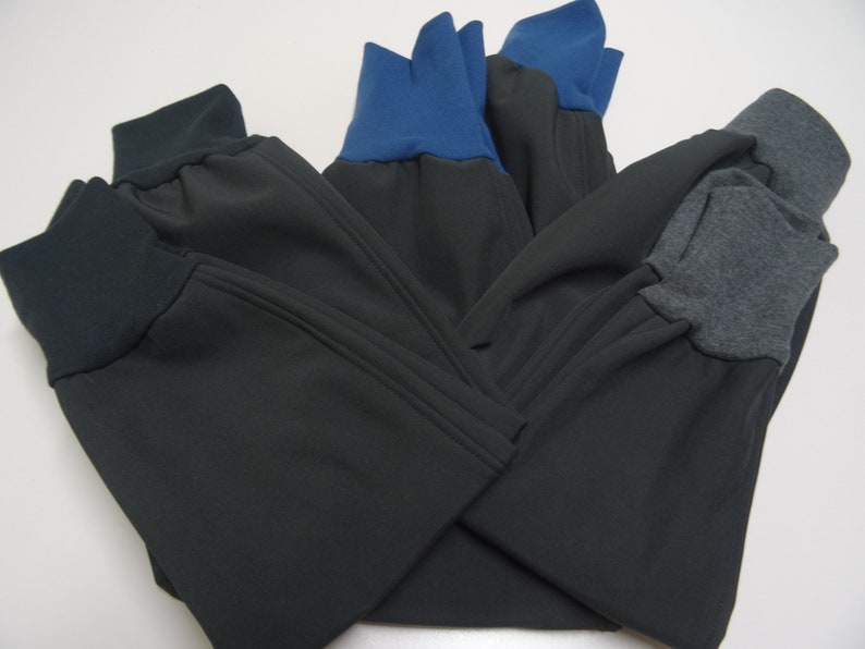 May include: Three pairs of black sweatpants with different colored cuffs. One pair has blue cuffs, one pair has gray cuffs, and one pair has black cuffs.