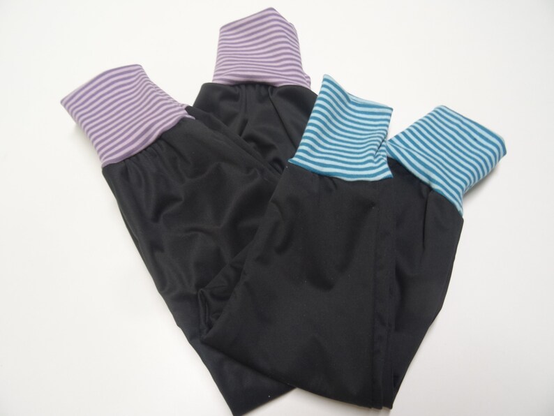 May include: Three pairs of black leggings with different colored striped cuffs. The cuffs are purple, blue, and teal.