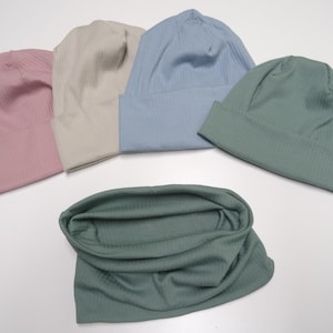 Könnte beinhalten: Vier gerippte Strickmützen in Rosa, Beige, Blau und Grün sowie ein passender grüner gerippter Strick-Halswärmer.