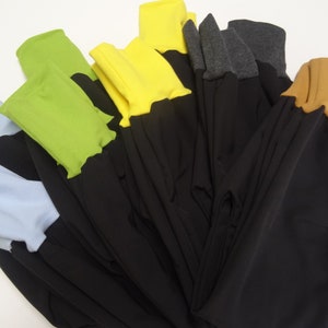 May include: A stack of black pants with different colored fabric trim. The trim colors include light blue, green, yellow, gray, and brown.