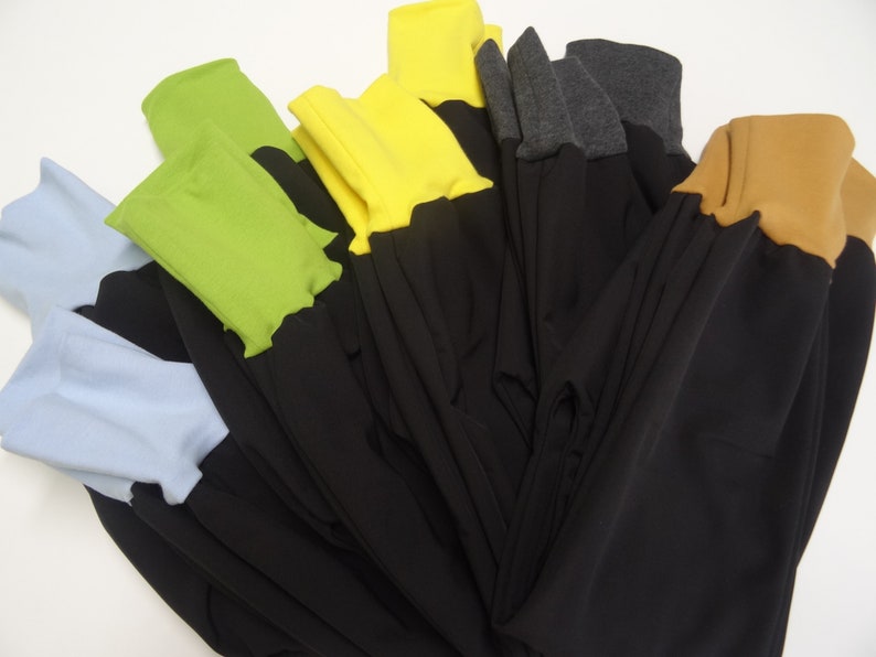 May include: A stack of black pants with different colored fabric trim. The trim colors include light blue, green, yellow, gray, and brown.