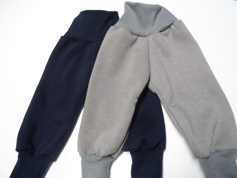 以下が含まれることがあります： グレーとネイビーの2本のスウェットパンツ。両方のパンツは、ゴム製のギャザーウエストバンドとカフ付きのレッグを持っています。