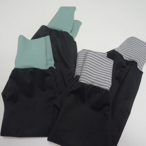 May include: Three pairs of black pants with different colored fabric trim. One pair has a green trim, one has a gray and white striped trim, and one has a solid green trim.