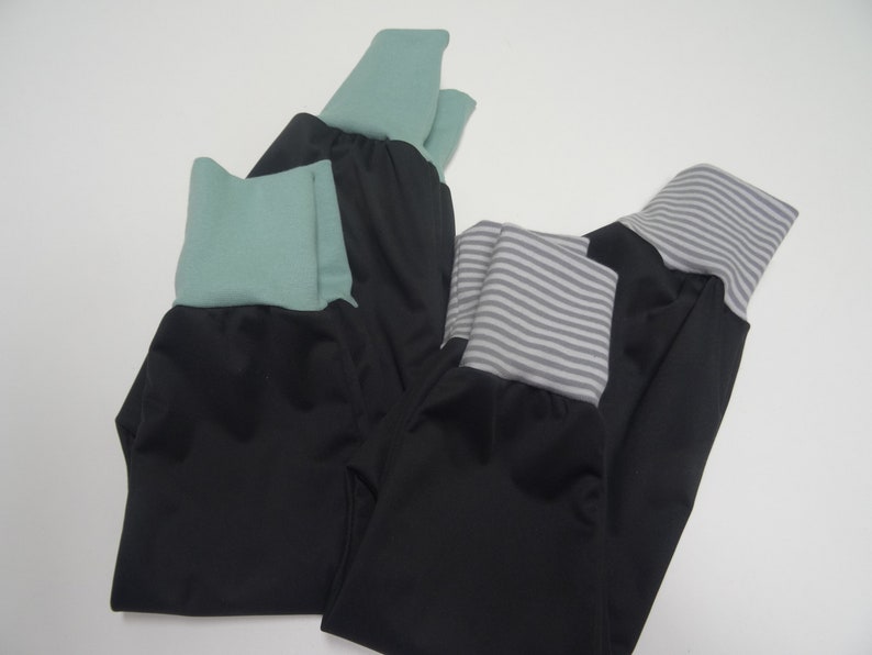 May include: Three pairs of black pants with different colored fabric trim. One pair has a green trim, one has a gray and white striped trim, and one has a solid green trim.