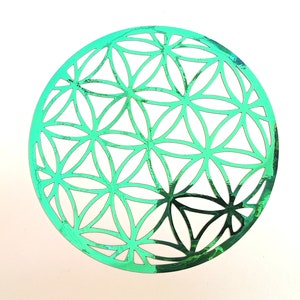 Puede incluir: Una pegatina metálica verde iridiscente con un diseño de flor de la vida. La pegatina es circular y tiene un patrón detallado de círculos superpuestos.