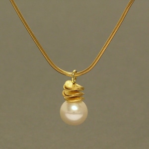 Op de afbeelding: Een gouden ketting met een hanger bestaande uit een stapel gouden schijven met daarop een witte parel.