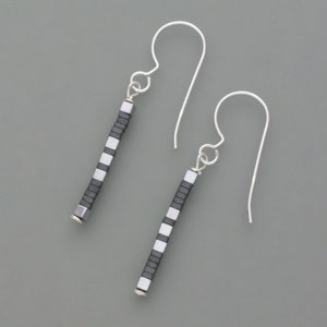 Könnte beinhalten: Ein Paar silberne Ohrhänger mit schwarzen und weißen quadratischen Perlen. Die Ohrringe sind aus Sterlingsilber gefertigt und haben ein schlichtes, elegantes Design.