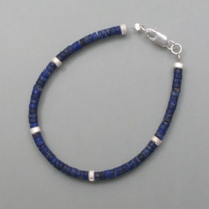 Pode incluir: Um bracelete de contas de lapis-lazúli azul com detalhes prateados e fecho de lagosta.