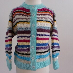 Könnte beinhalten: Ein bunter gestreifter Cardigan mit einem hellblauen Knopfleisten vorne. Der Cardigan ist aus weichem, gestricktem Stoff gefertigt und in verschiedenen Farben gehalten, darunter Rot, Orange, Gelb, Grün, Blau, Lila und Weiß.