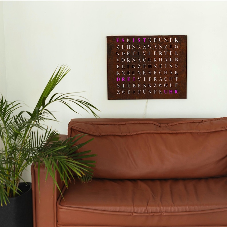 May include: A rusty metal wall art piece with the words "ES KIST FUNK ZEHNKZWANZIG DREIVIERTEL VOR NACH HALB ELF ZEHNEINS NEUNKSECHS DREIVIERECHT SIEBENKZWOL ZWEIFUNKUHR" written in pink.