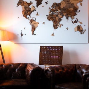 May include: A brown leather couch with a wooden world map hanging on the wall behind it. A metal sign with the word "SECHS" in pink letters is on a stand in front of the couch.