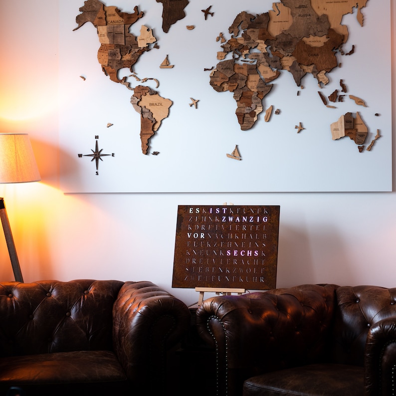 May include: A brown leather couch with a wooden world map hanging on the wall behind it. A metal sign with the word "SECHS" in pink letters is on a stand in front of the couch.