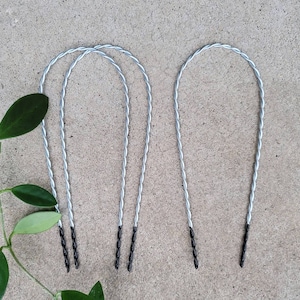 May include: Three silver plant supports with black tips. The supports are bent into a U-shape and are made of twisted wire.