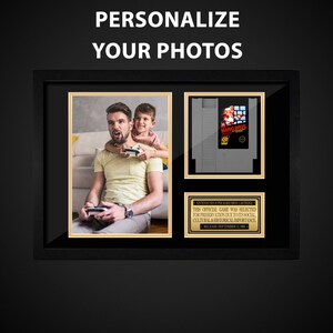 Peut inclure: Un collage de photos encadré représentant un père et son fils jouant à un jeu vidéo, avec une cartouche vintage de Nintendo Super Mario Bros. exposée à côté d'eux. Le cadre a une bordure noire et un passe-partout doré.