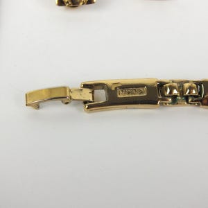 K&ouml;nnte beinhalten: Nahaufnahme eines goldfarbenen Halskettenverschlusses mit dem Markennamen "Monet". Der Verschluss ist rechteckig und verbindet sich mit einer passenden Goldkette. Der Schmuck ist vor einem wei&szlig;en Hintergrund platziert.