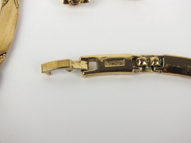 K&ouml;nnte beinhalten: Nahaufnahme eines goldfarbenen Halskettenverschlusses mit dem Markennamen "Monet". Der Verschluss ist rechteckig und verbindet sich mit einer passenden Goldkette. Der Schmuck ist vor einem wei&szlig;en Hintergrund platziert.