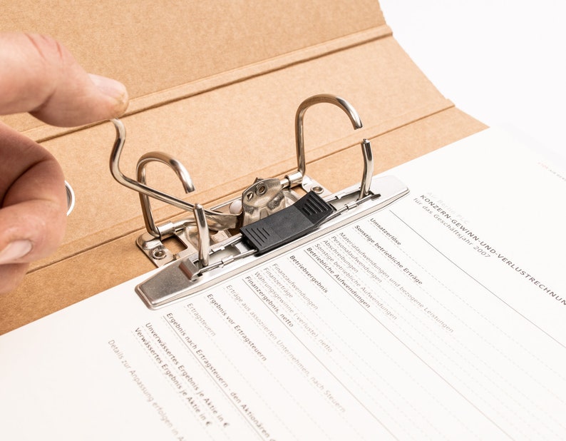 May include: A brown cardboard binder with a metal mechanism for holding papers. The binder is open and the metal mechanism is visible. The text on the page reads "KONZERN-GEWINN-UND-VERLUSTRECHNUN" and "F&uuml;r das Gesch&auml;ftsjahr 2007".