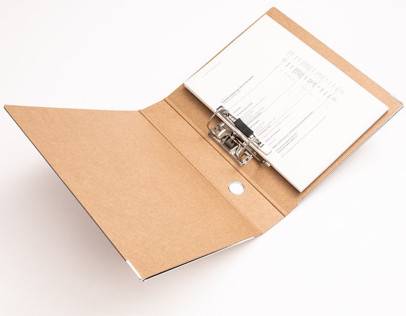 May include: A brown cardboard file folder with a metal ring binder and a white sheet of paper inside. The folder is open and the paper is visible.