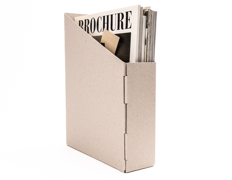 May include: A beige cardboard magazine holder with a stack of magazines inside. The top magazine has the word "BROCHURE" printed on the cover.