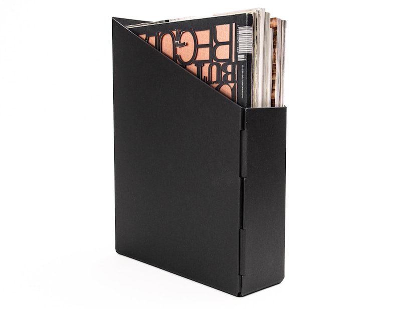May include: Black magazine holder with a triangular opening. The holder is made of a sturdy material and has a sleek, modern design.