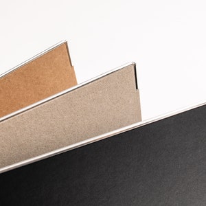May include: Three cardboard folders with silver edges. The top folder is brown, the middle folder is grey, and the bottom folder is black.