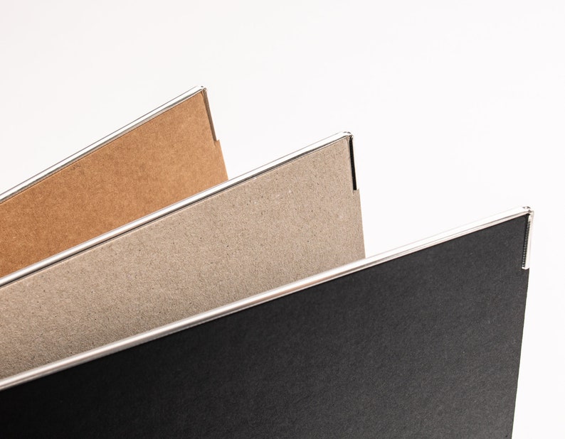 May include: Three cardboard folders with silver edges. The top folder is brown, the middle folder is grey, and the bottom folder is black.