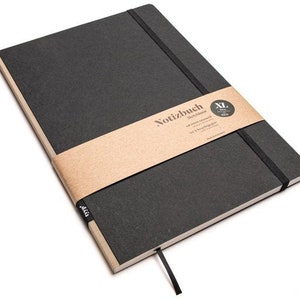 Könnte beinhalten: Ein schwarzes XL-Skizzenbuch mit einem beigefarbenen Papierband und einem schwarzen Gummibandverschluss. Der Einband ist dunkelgrau und die Seiten sind cremefarben. Der Text "Notizbuch sketchbook" ist auf dem Band aufgedruckt. Ein schwarzes Lesebändchen ist angebracht.