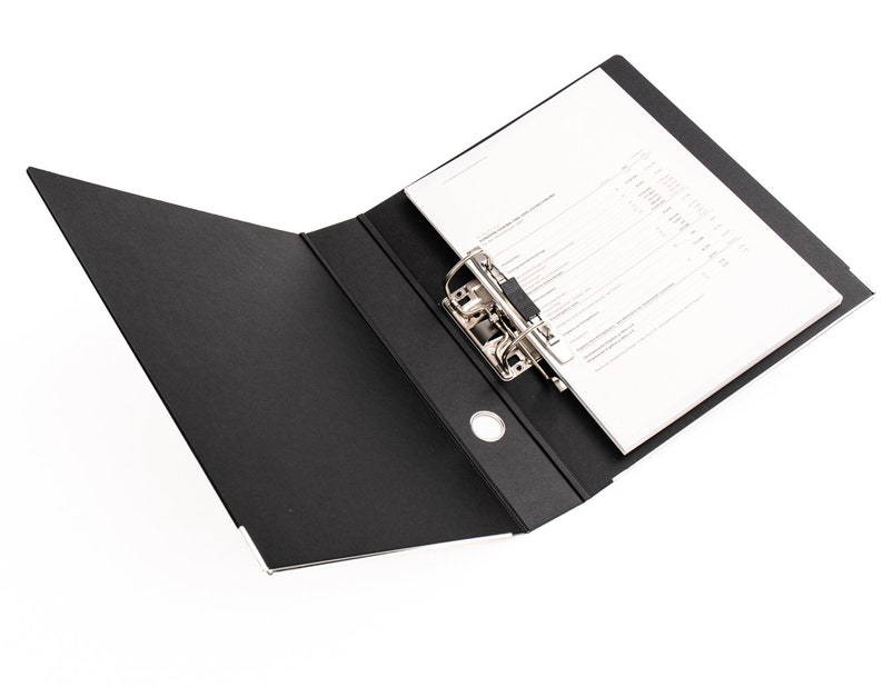 May include: A black binder with a silver metal ring mechanism. The binder is open and has a white sheet of paper inserted.