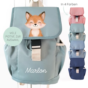 Könnte beinhalten: Ein tealfarbener Rucksack mit einer Cartoon-Fuchs-Illustration auf der Klappe. Der Rucksack hat einen weißen Riemen, eine schwarze Schnalle und den Namen "Marlon" in weißer Schrift. Zusätzliche Rucksäcke in Pink, Hellblau, Mittelblau und Marineblau werden gezeigt.